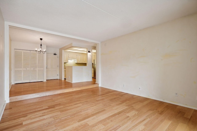 spare room with a notable chandelier and light hardwood / wood-style floors