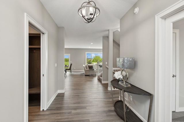 hallway featuring a notable chandelier, dark wood-style flooring, and baseboards