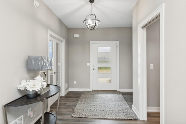 entrance foyer featuring a notable chandelier, dark wood finished floors, visible vents, and baseboards