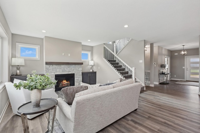 living room with recessed lighting, dark wood-type flooring, a stone fireplace, baseboards, and stairs