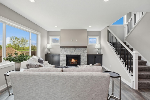 living room featuring baseboards, wood finished floors, stairs, a stone fireplace, and recessed lighting