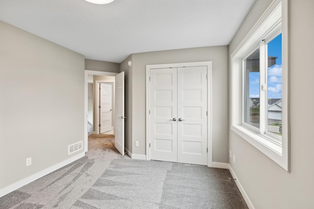 unfurnished bedroom featuring light colored carpet, a closet, visible vents, and baseboards