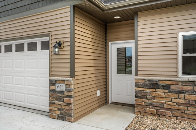 view of exterior entry featuring stone siding, a shingled roof, and a garage