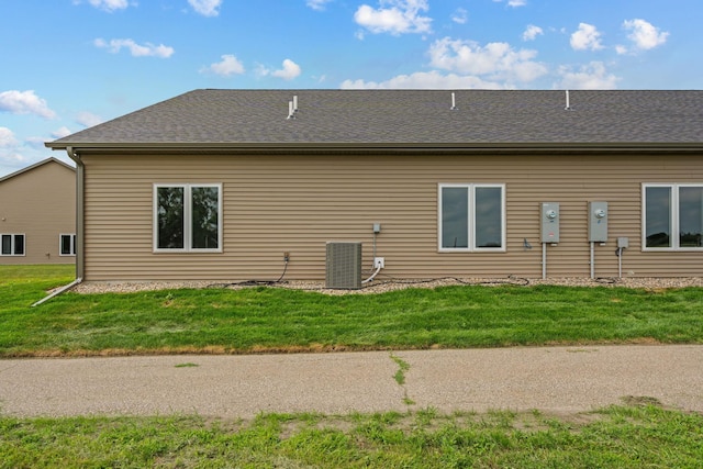 back of property featuring cooling unit, a lawn, and a shingled roof