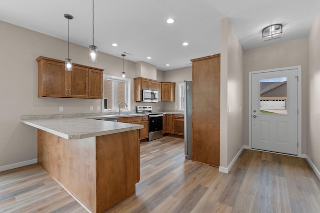 kitchen with brown cabinets, appliances with stainless steel finishes, a peninsula, light wood-style floors, and a sink