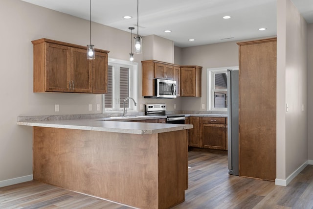 kitchen featuring brown cabinets, a peninsula, stainless steel appliances, and wood finished floors