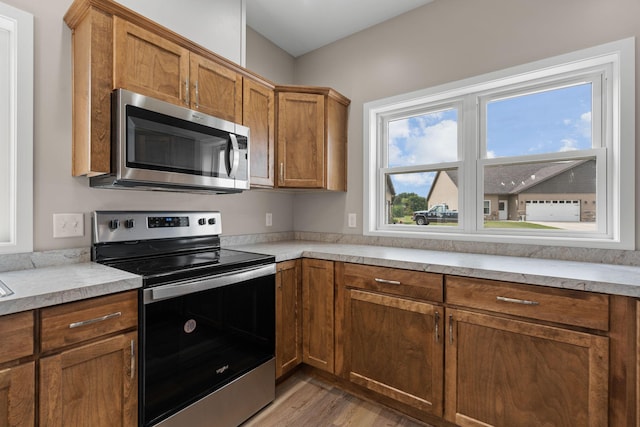 kitchen with light wood-type flooring, stainless steel appliances, brown cabinets, and light countertops