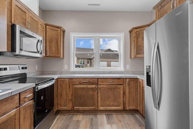 kitchen with light wood finished floors, visible vents, brown cabinets, and appliances with stainless steel finishes