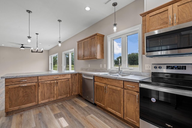 kitchen with a sink, stainless steel appliances, light wood-style floors, a peninsula, and brown cabinetry