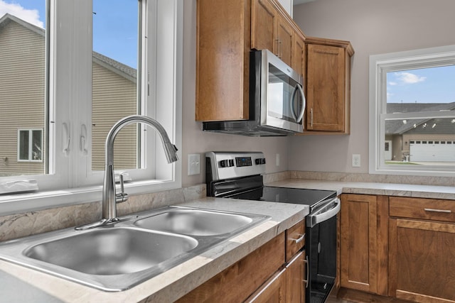 kitchen with a sink, brown cabinets, a wealth of natural light, and stainless steel appliances