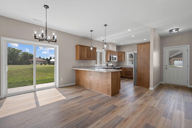 kitchen featuring brown cabinetry, appliances with stainless steel finishes, a peninsula, and light wood-style floors