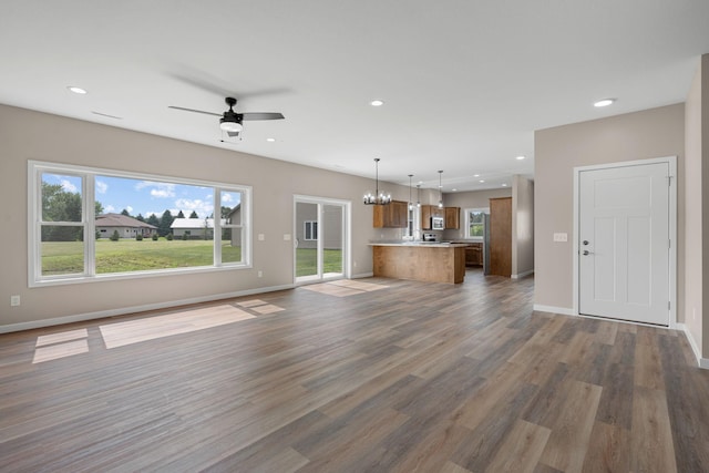 unfurnished living room with recessed lighting, baseboards, wood finished floors, and ceiling fan with notable chandelier