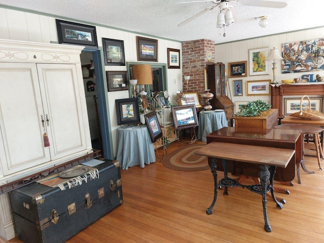 dining space featuring light hardwood / wood-style flooring, ceiling fan, brick wall, and a textured ceiling