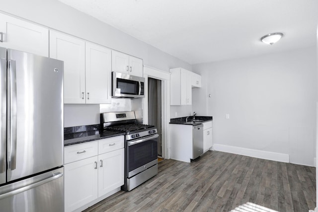 kitchen featuring sink, appliances with stainless steel finishes, white cabinetry, dark stone countertops, and dark hardwood / wood-style flooring