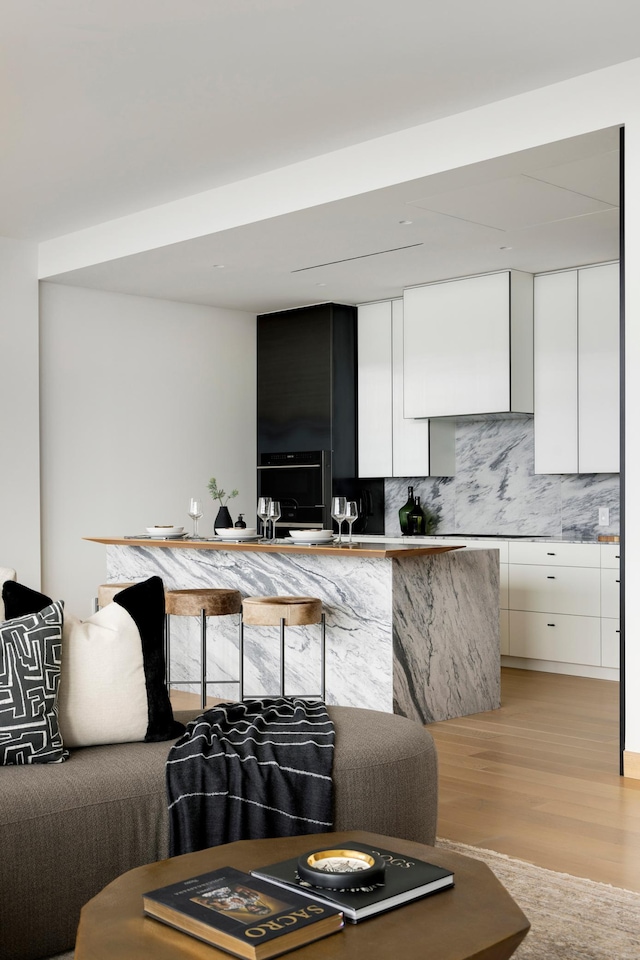 kitchen with white cabinets, black oven, light hardwood / wood-style floors, and backsplash