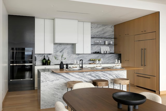 kitchen with white cabinetry, a kitchen breakfast bar, light hardwood / wood-style flooring, an island with sink, and decorative backsplash