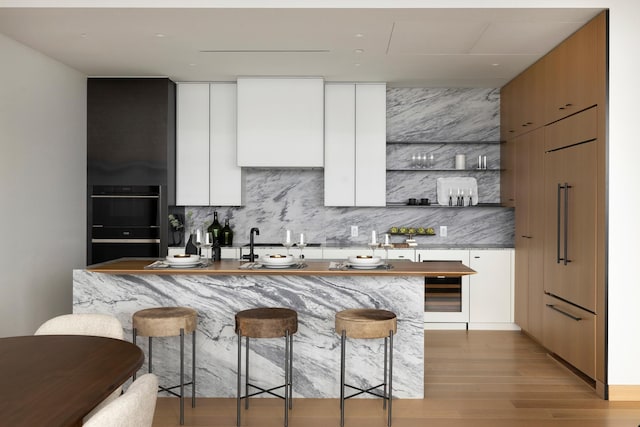 kitchen featuring white cabinets, light wood-type flooring, a kitchen bar, and black double oven