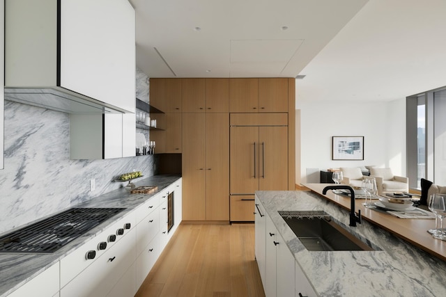 kitchen with light wood-type flooring, backsplash, paneled fridge, sink, and white cabinets