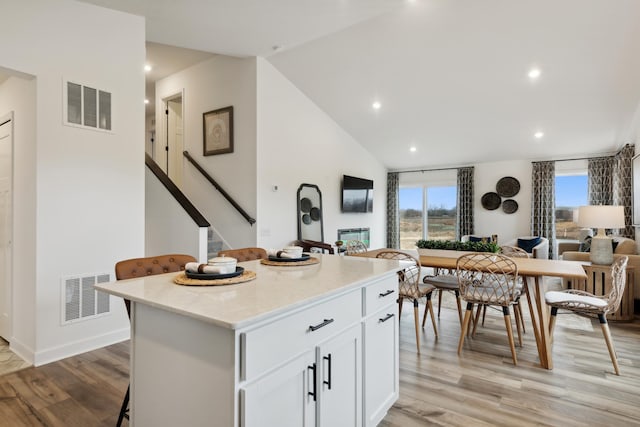 kitchen with light hardwood / wood-style flooring, vaulted ceiling, white cabinets, a kitchen bar, and a center island