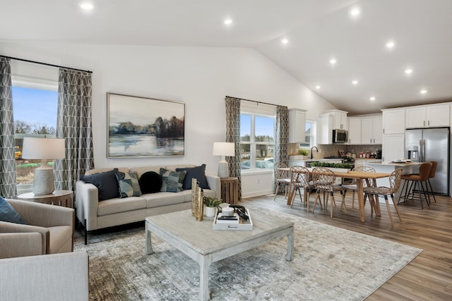 living room with high vaulted ceiling, sink, and light hardwood / wood-style floors