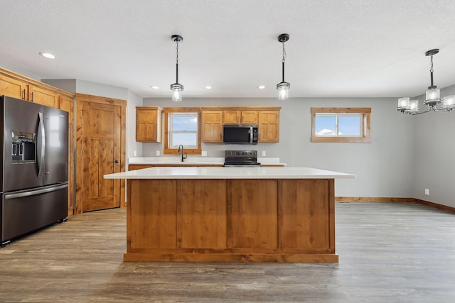 kitchen with a center island, stainless steel appliances, an inviting chandelier, pendant lighting, and light wood-type flooring