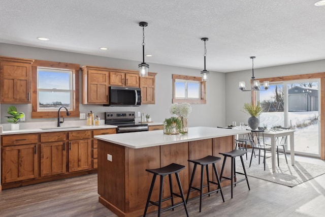 kitchen with sink, a breakfast bar area, hanging light fixtures, a kitchen island, and electric stove