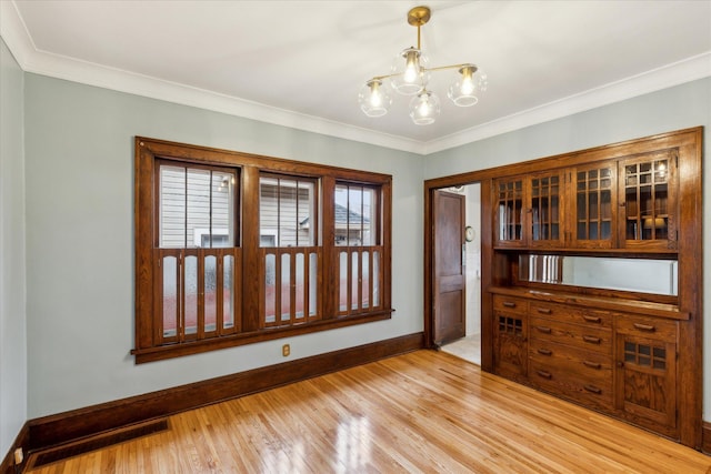 unfurnished room featuring an inviting chandelier, ornamental molding, and light hardwood / wood-style flooring