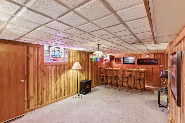 bar with wood walls, a paneled ceiling, and light carpet