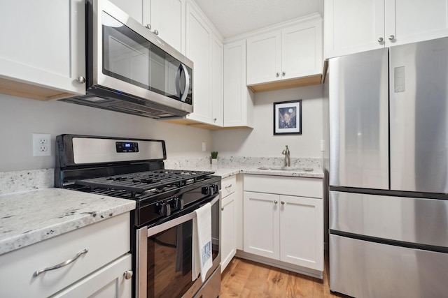 kitchen featuring white cabinets, light stone countertops, light wood-type flooring, stainless steel appliances, and sink