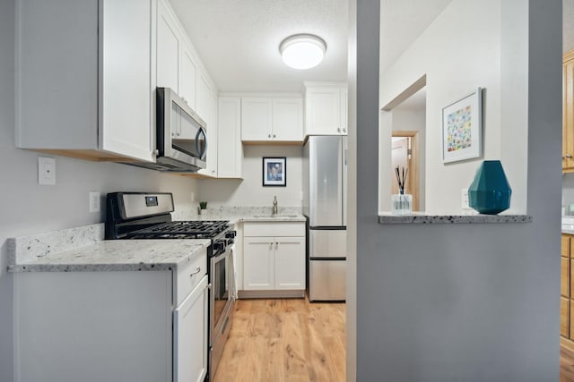 kitchen featuring light stone counters, white cabinets, stainless steel appliances, and light hardwood / wood-style floors