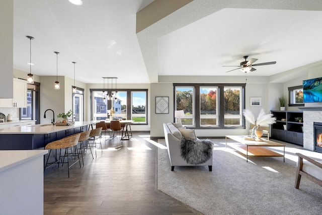 living room with a fireplace, dark hardwood / wood-style floors, sink, a textured ceiling, and ceiling fan with notable chandelier