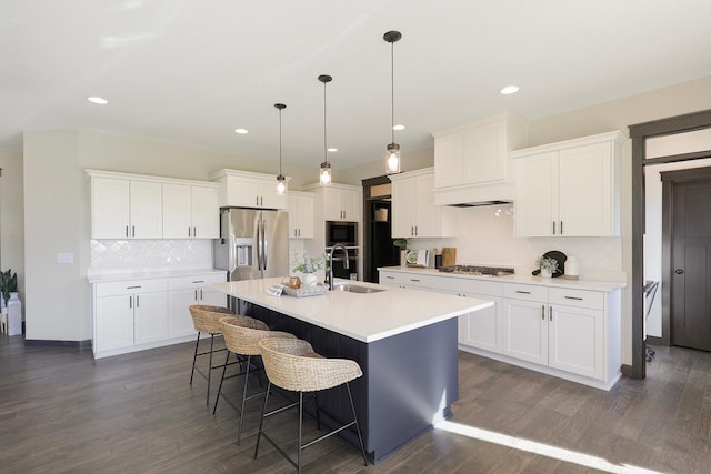 kitchen with appliances with stainless steel finishes, white cabinetry, a kitchen island with sink, dark hardwood / wood-style floors, and sink