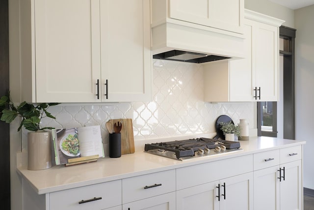 kitchen with stainless steel gas cooktop, tasteful backsplash, custom exhaust hood, and white cabinets