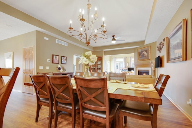 dining room with ceiling fan with notable chandelier and light wood-type flooring