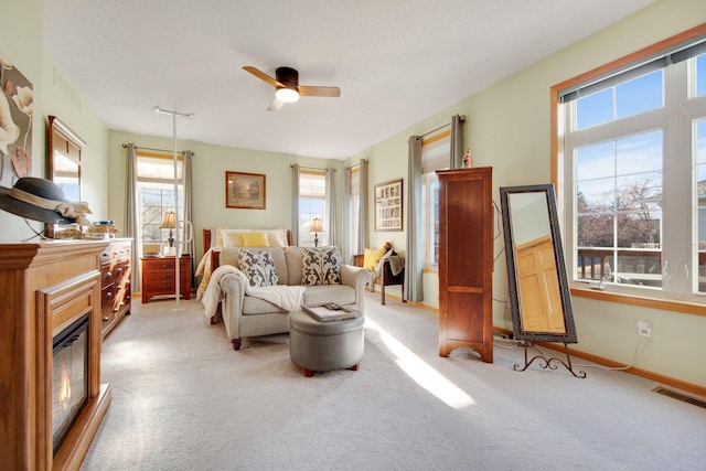 living area featuring light colored carpet, ceiling fan, and a healthy amount of sunlight