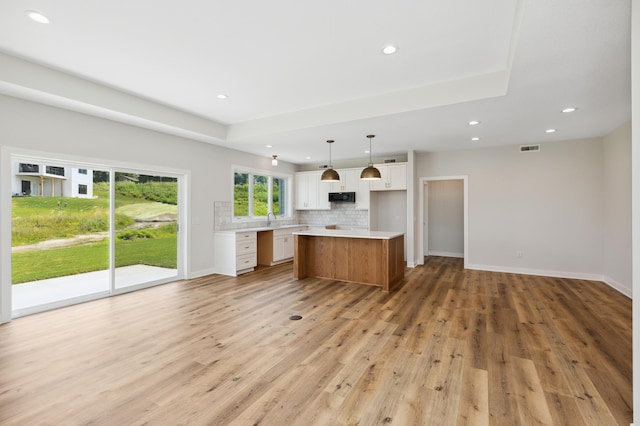 kitchen with white cabinets, hanging light fixtures, light hardwood / wood-style flooring, tasteful backsplash, and a kitchen island