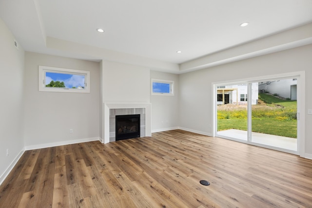 unfurnished living room featuring a raised ceiling, a tile fireplace, and hardwood / wood-style flooring