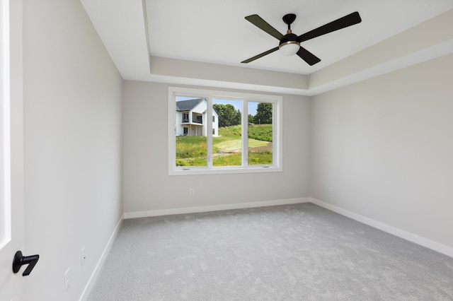 empty room featuring a raised ceiling, ceiling fan, and light colored carpet