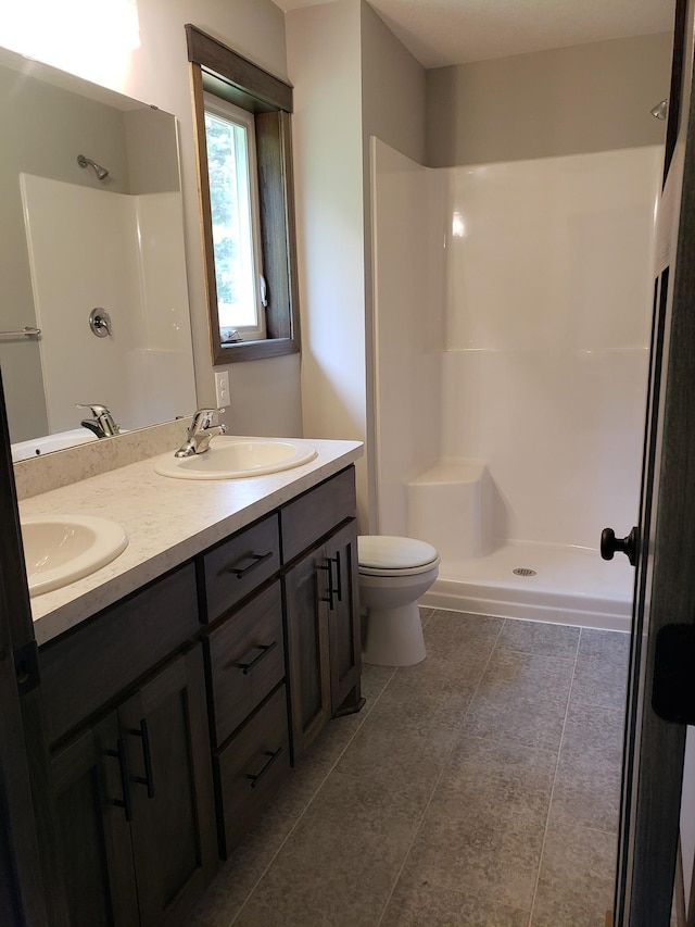 bathroom with tile flooring, toilet, double vanity, and a shower