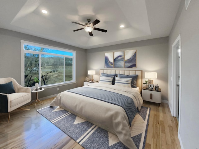 bedroom featuring ceiling fan, a raised ceiling, and light wood-type flooring