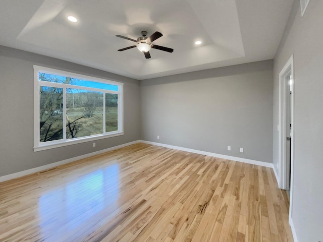 empty room featuring ceiling fan, a raised ceiling, and light wood-type flooring