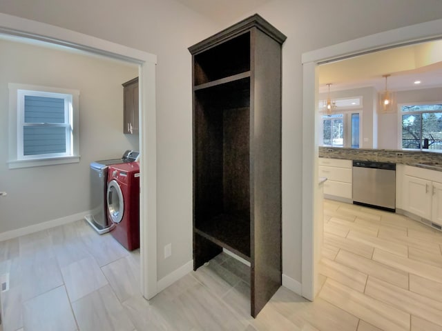 clothes washing area featuring washer and dryer, a chandelier, and cabinets