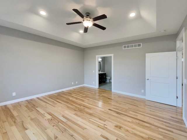 interior space featuring ceiling fan, light hardwood / wood-style floors, connected bathroom, and a tray ceiling