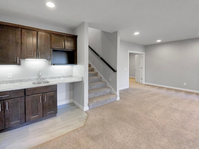 kitchen featuring light carpet, dark brown cabinets, light stone counters, and sink