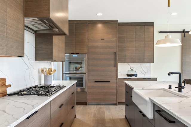 kitchen featuring decorative light fixtures, sink, stainless steel appliances, light stone countertops, and custom range hood