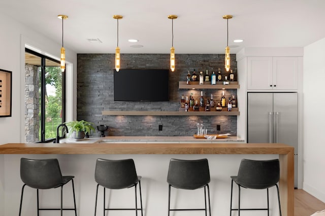 bar featuring hanging light fixtures, white cabinets, and stainless steel built in refrigerator