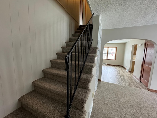 stairs with carpet floors and a textured ceiling