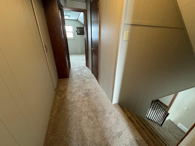 corridor with a wall mounted air conditioner, light colored carpet, lofted ceiling, and wooden walls