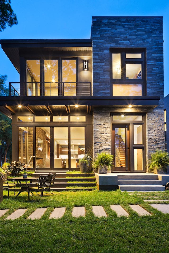 rear view of house with a yard, stone siding, and a balcony