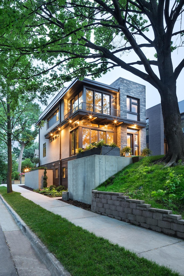 modern home featuring a front yard, stone siding, and a balcony